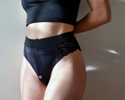 Black lace strap-on harness underwear — front view worn — Ma Joie. A person wearing a black harness lingerie with lace detailing on the waist. The harness is designed to hold accessories for intimate activities.